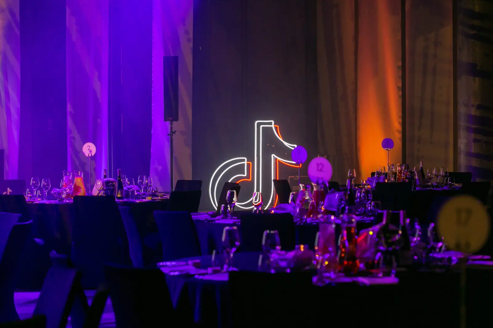 Numbered set tables in purple light, with a partner's glowing neon sign in the background — DMR Gala X (2021)