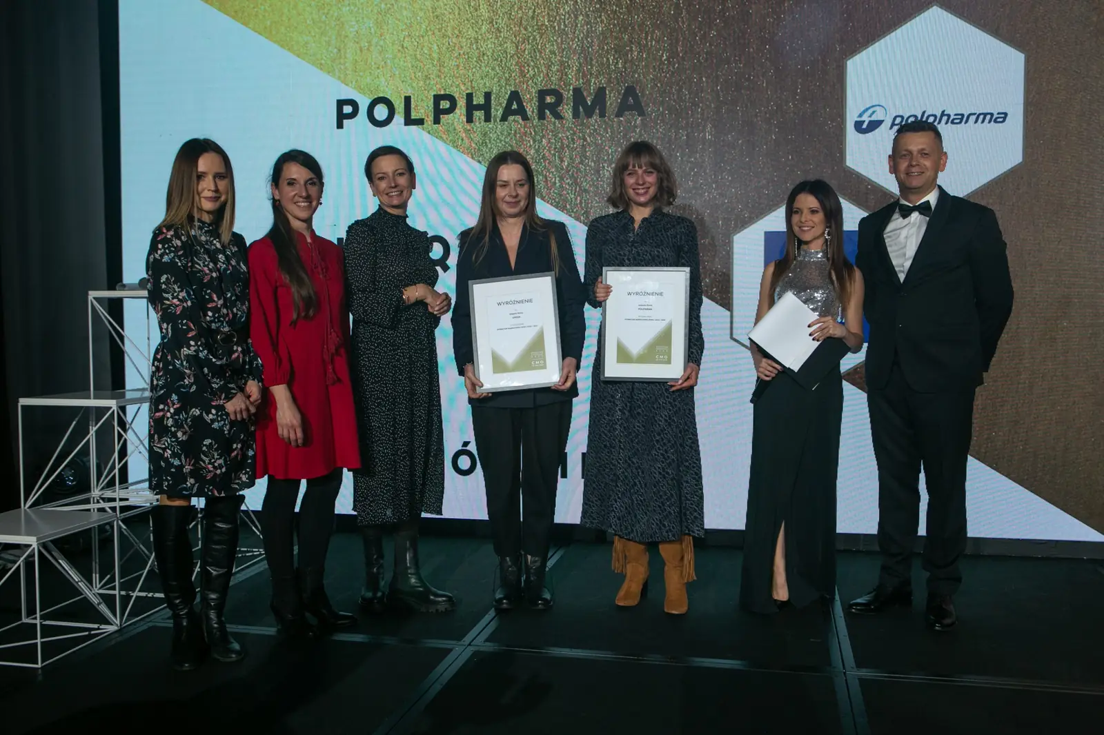 Seven women from an awarded team pose with diplomas next to the host in a tuxedo — DMR Gala X (2021)