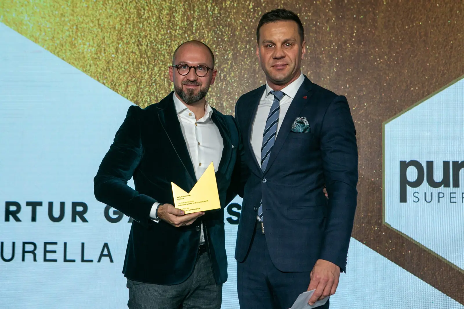 Winner in glasses with a golden statuette poses next to the presenter in a navy suit — DMR Gala X (2021)