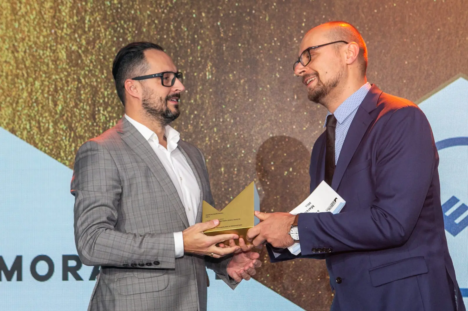 Smiling winner in a grey checked suit receives the statuette from the presenter in glasses — DMR Gala X (2021)