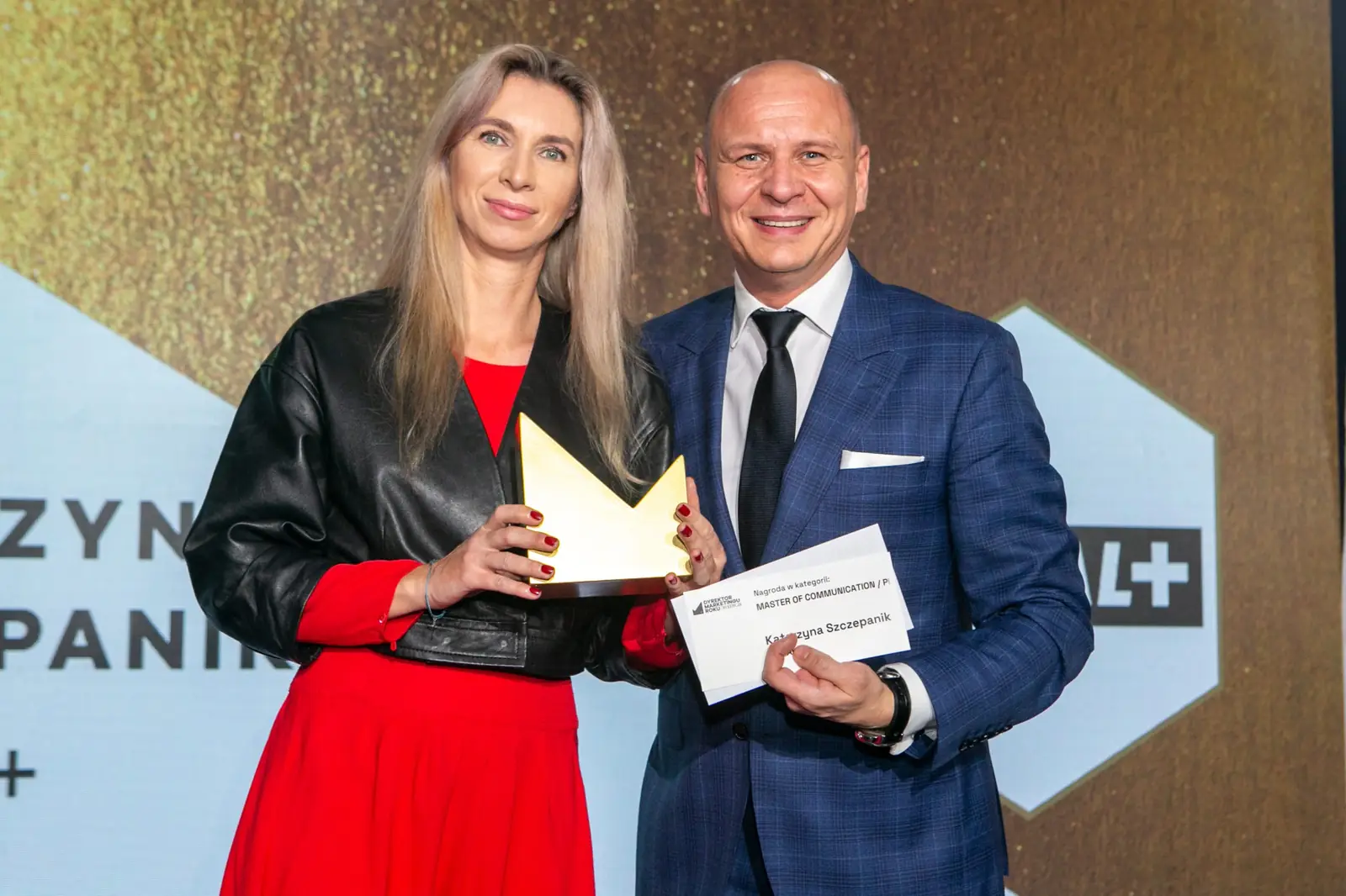 Winner in a red dress and leather jacket poses with her statuette beside the presenter — DMR Gala X (2021)