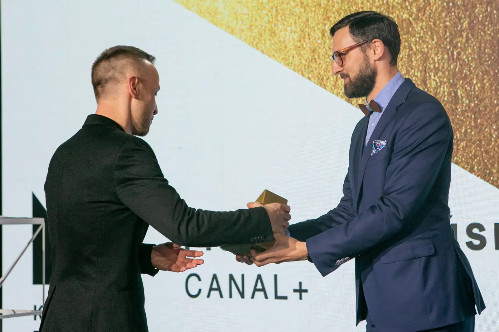 Bearded presenter in glasses hands the statuette to a winner in a black jacket — DMR Gala X (2021)