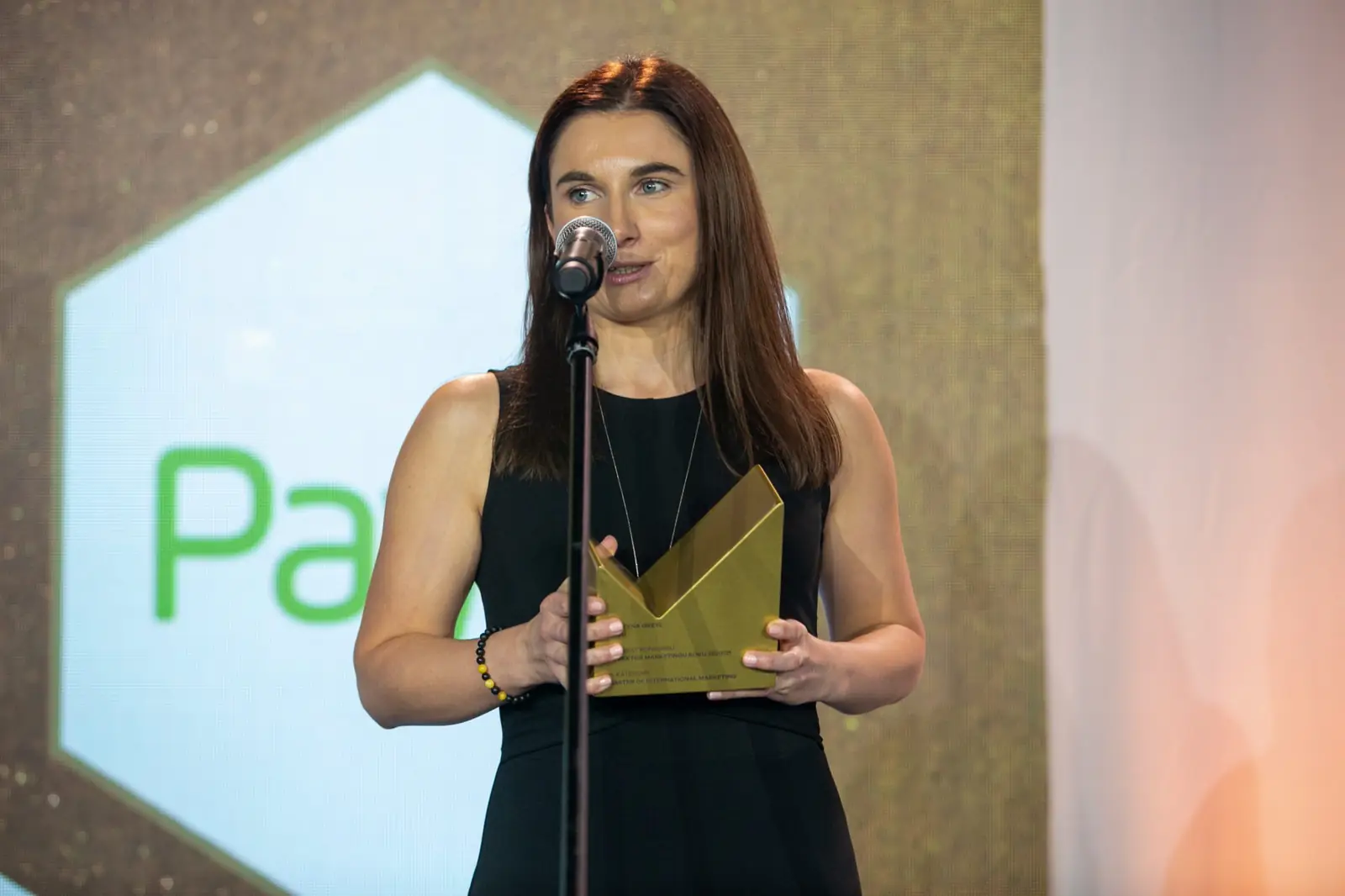 Winner in a sleeveless black dress speaks at the microphone holding her statuette — DMR Gala X (2021)