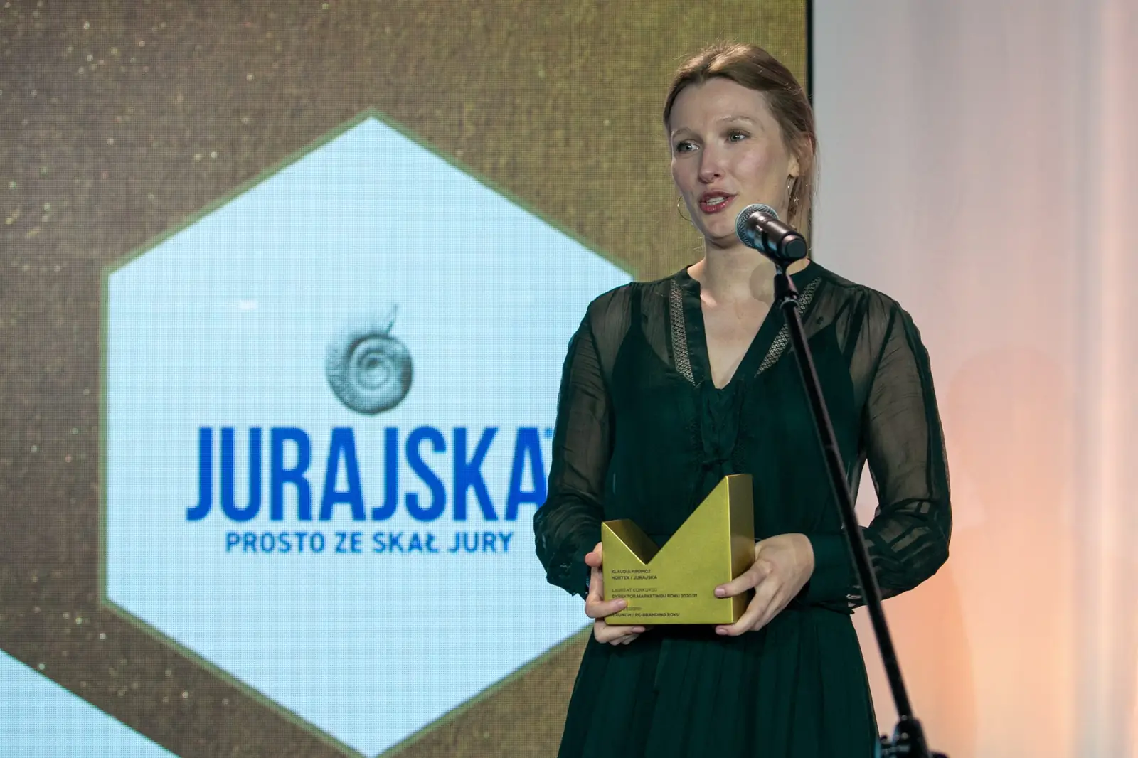 Winner with her hair up, in a dress with sheer sleeves, speaks into the microphone — DMR Gala X (2021)