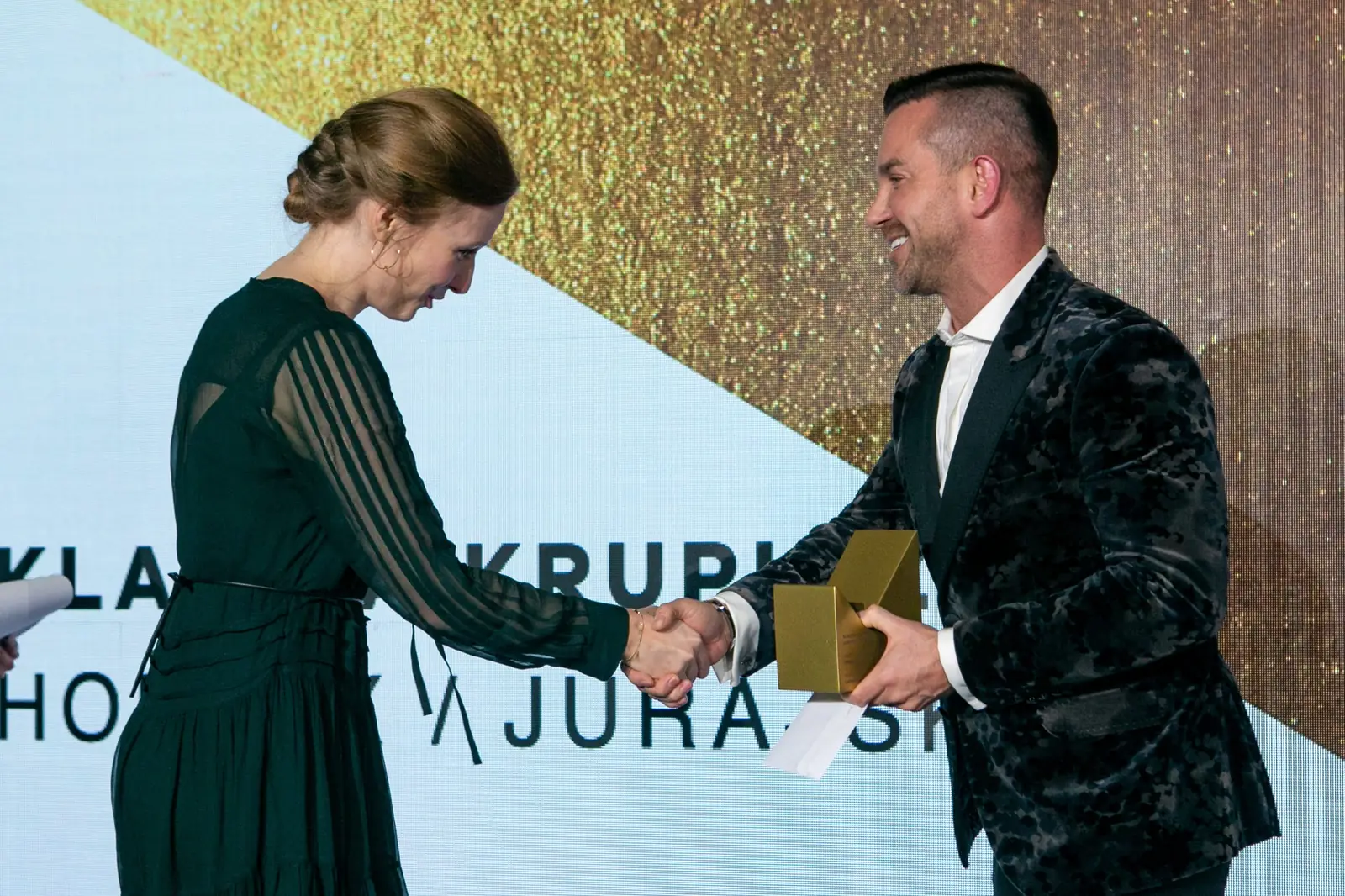 Winner in a dark green dress shakes the presenter's hand with a slight bow — DMR Gala X (2021)
