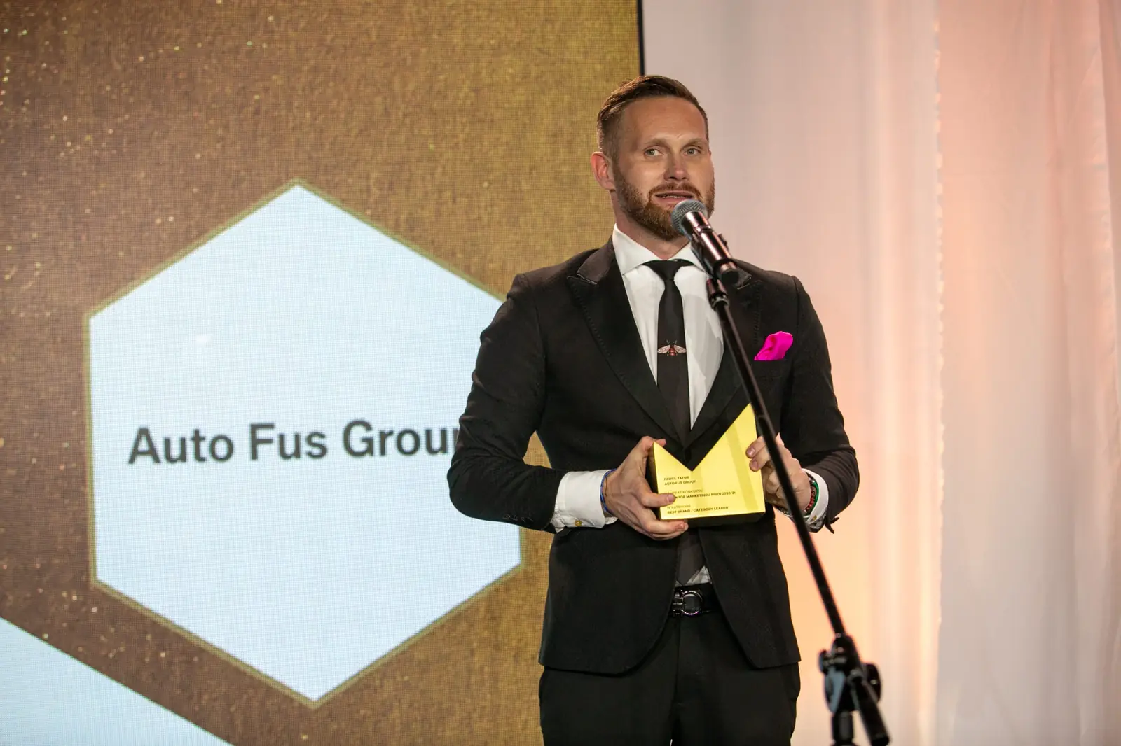 Laureat z różową poszetką przemawia przy mikrofonie, trzymając statuetkę oburącz — Gala DMR X (2021)