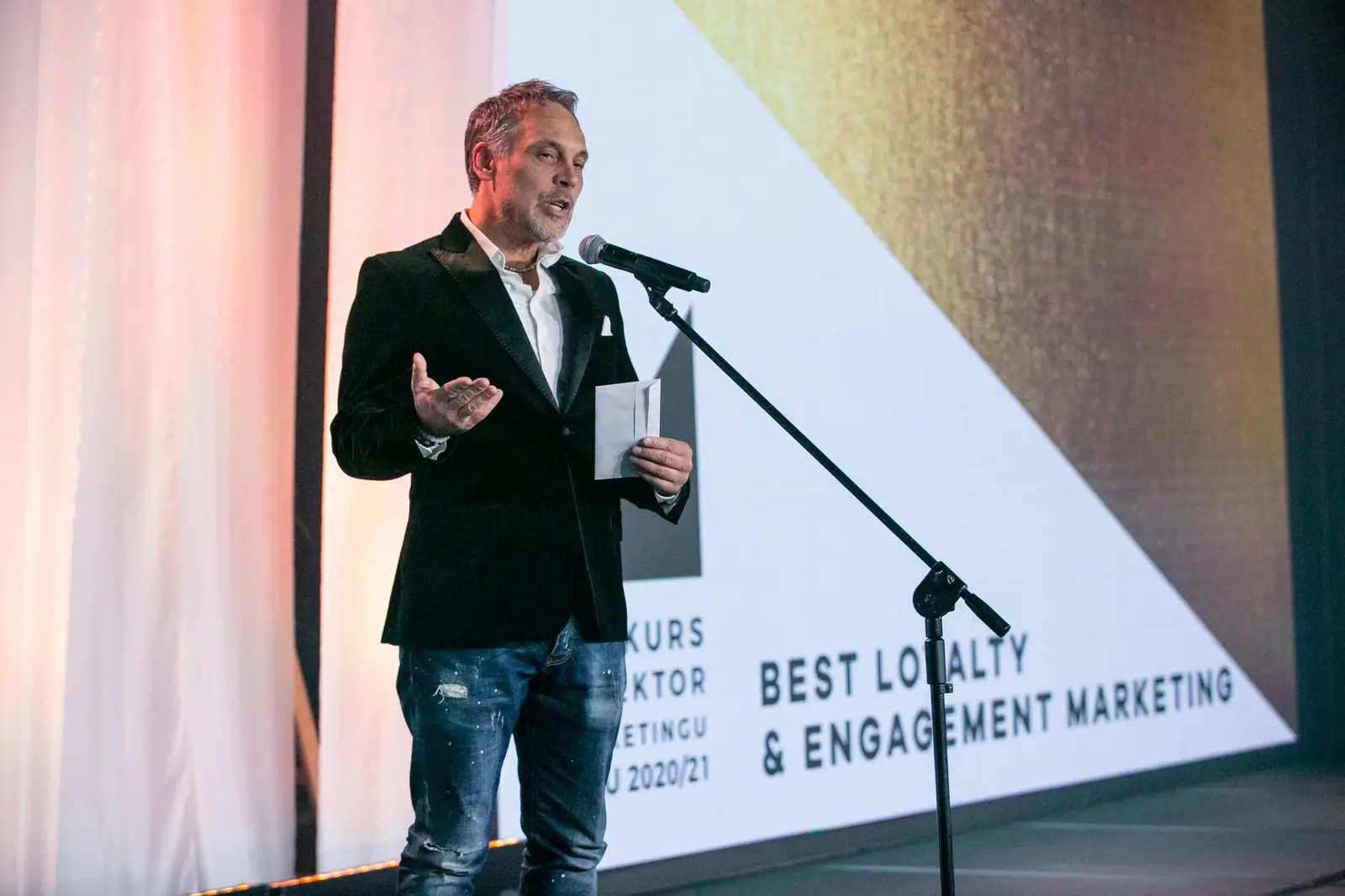 Presenter in a blazer and jeans announces the Best Loyalty & Engagement Marketing category — DMR Gala X (2021)