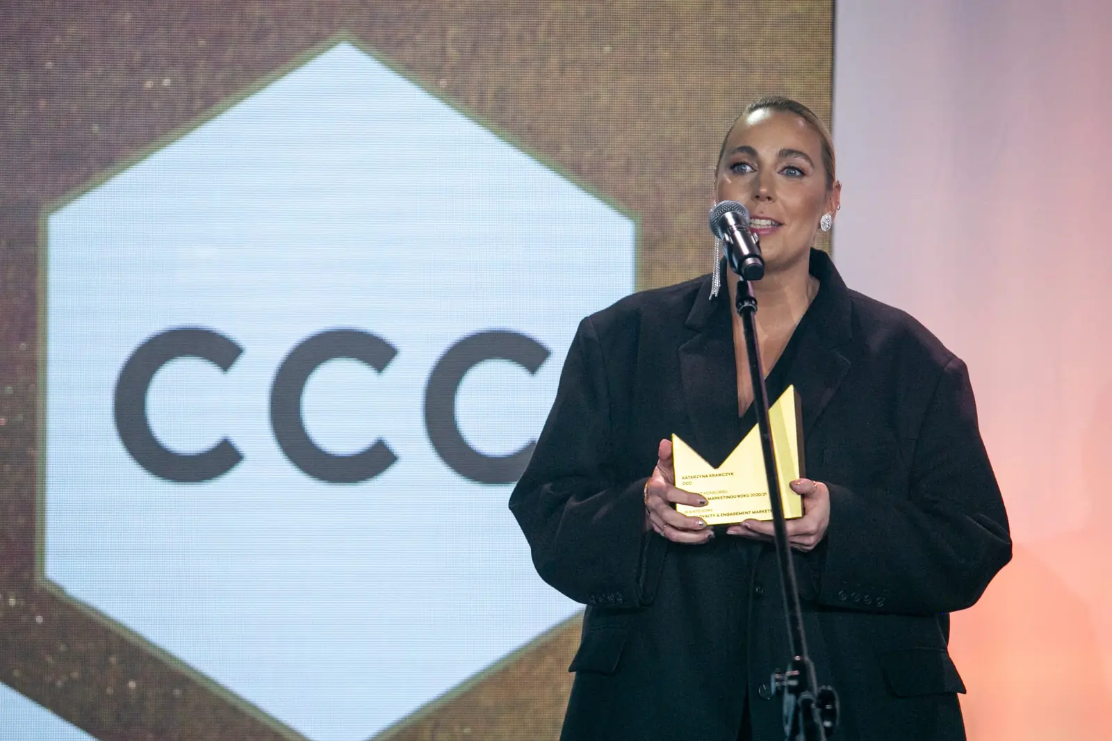 Winner in an oversized black blazer speaks at the microphone holding her statuette — DMR Gala X (2021)