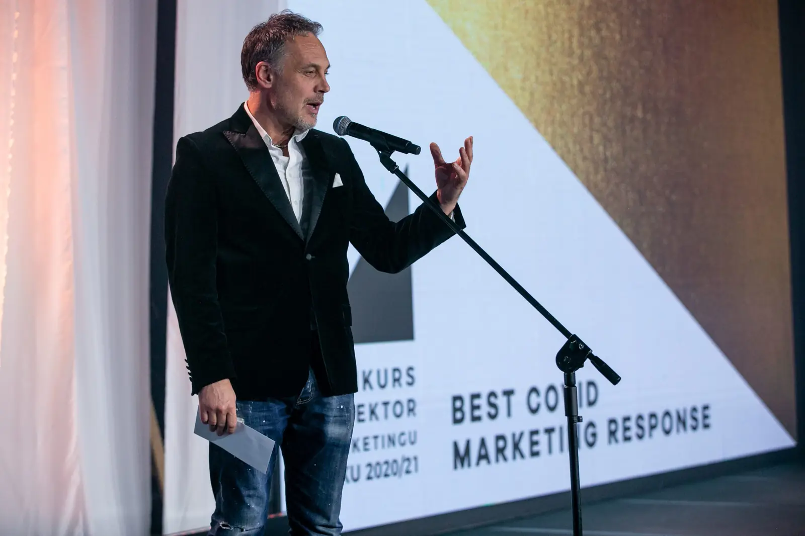 Wręczający z uniesioną dłonią zapowiada kategorię Best Covid Marketing Response — Gala DMR X (2021)