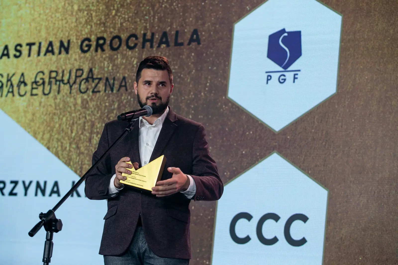 Bearded winner in a burgundy jacket gestures at the microphone with his statuette in hand — DMR Gala X (2021)