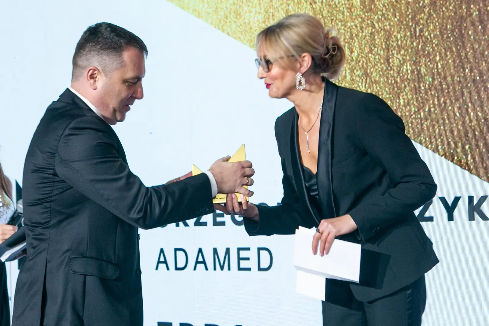 Presenter in glasses hands the statuette to a winner in a black suit — DMR Gala X (2021)