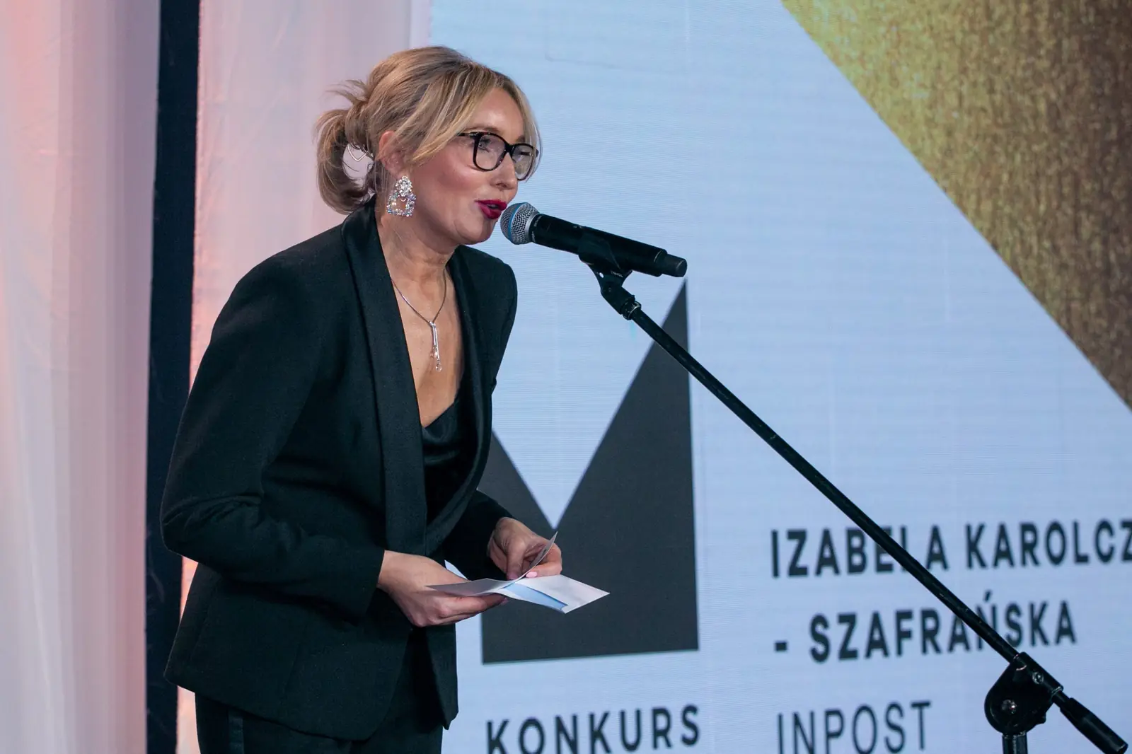 Presenter in glasses reads the next winner's name from a card — DMR Gala X (2021)