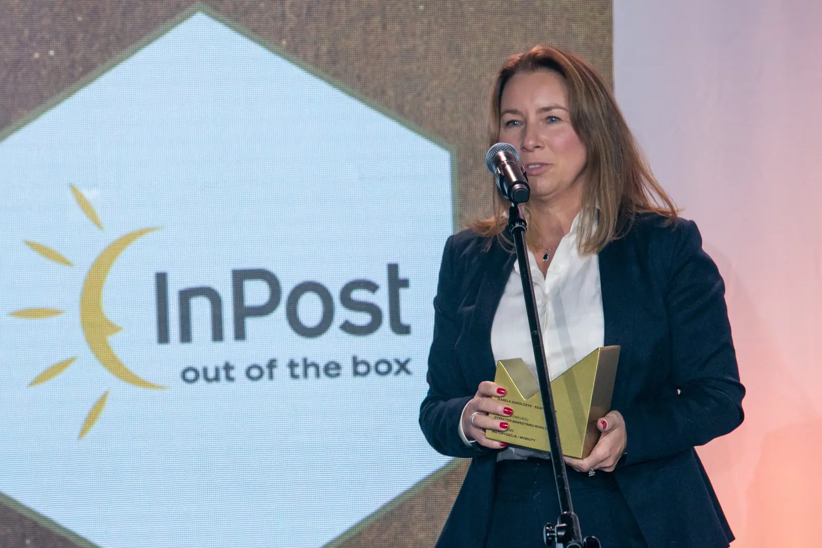 Winner in a navy blazer and white blouse speaks at the microphone holding her statuette — DMR Gala X (2021)