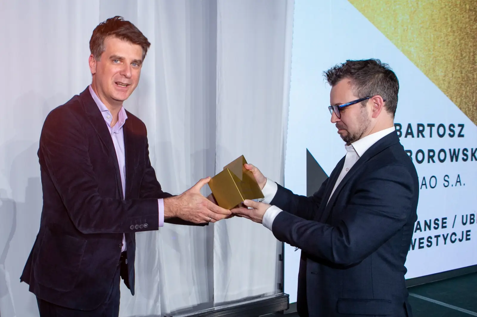 Presenter in a burgundy jacket hands the statuette to a winner in glasses — DMR Gala X (2021)