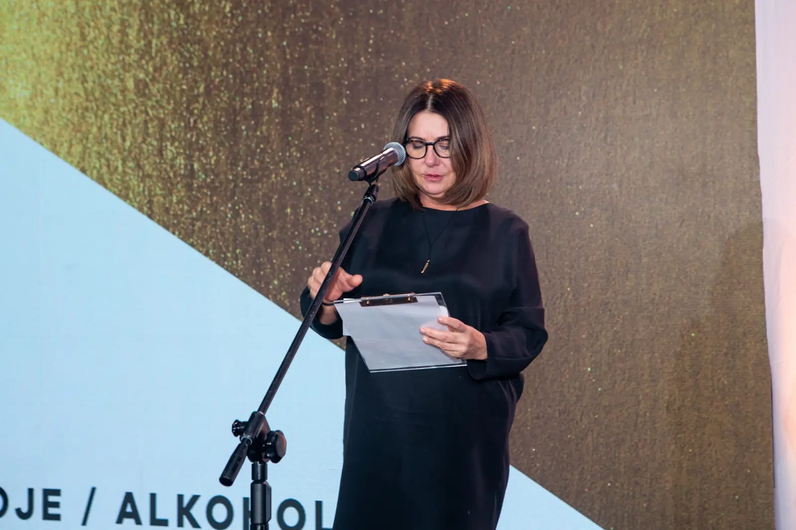 Presenter in glasses reads the verdict in the beverages and alcohol category from a clipboard — DMR Gala X (2021)