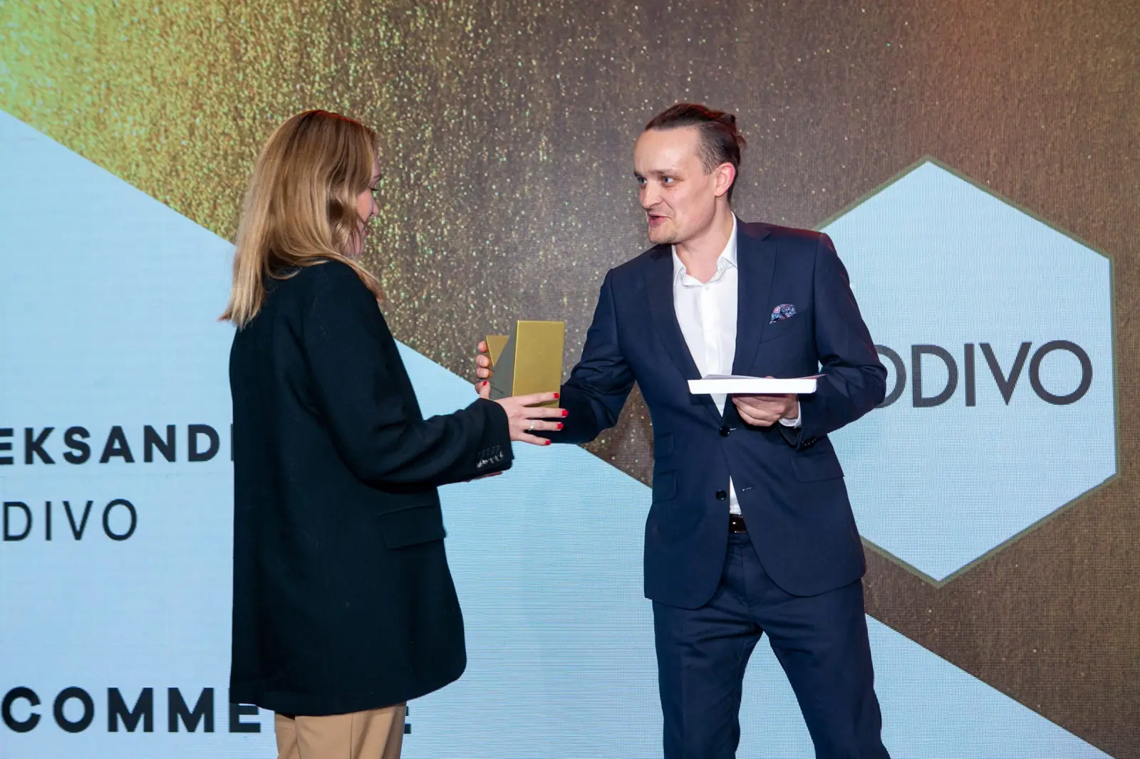 Wręczający z kokiem przekazuje statuetkę laureatce kategorii e-commerce — Gala DMR X (2021)