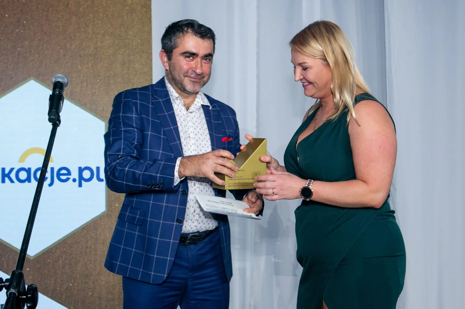Wręczający w marynarce w kratę podaje statuetkę laureatce w ciemnozielonej sukience — Gala DMR X (2021)