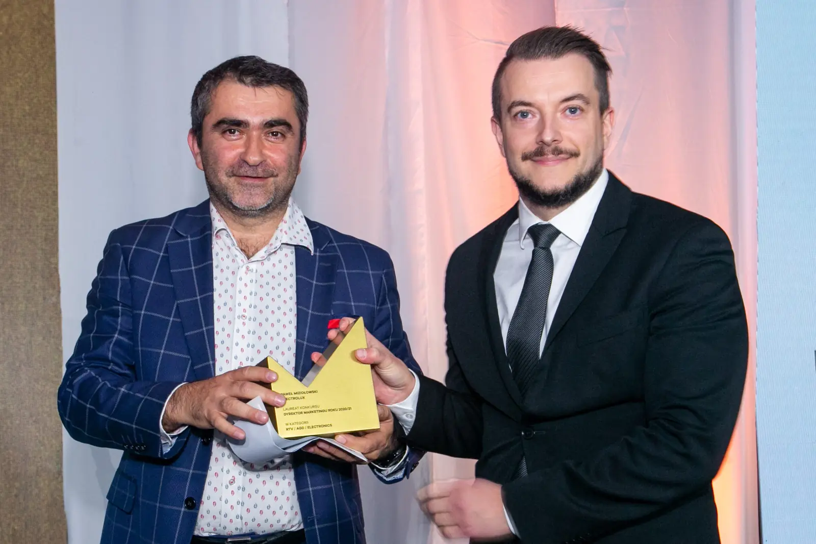 Moustached winner receives the statuette from the smiling presenter in a checked blazer — DMR Gala X (2021)