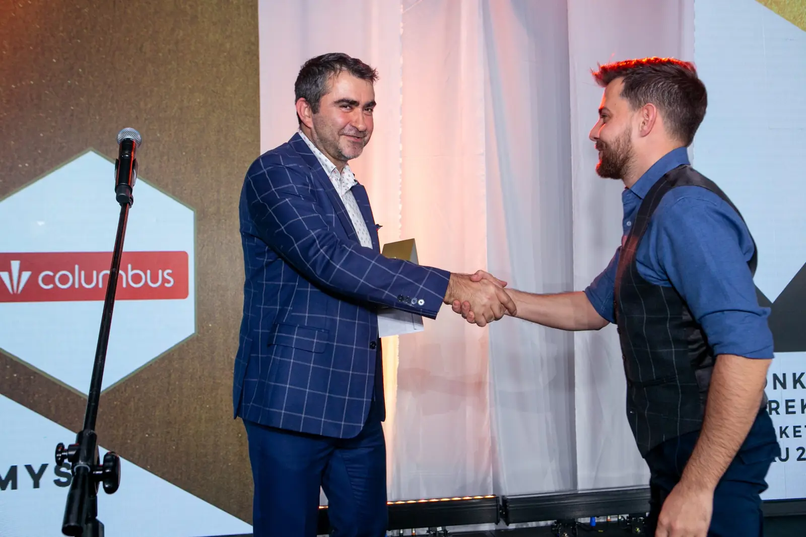 Presenter in a checked blazer shakes hands with a winner in a waistcoat and blue shirt — DMR Gala X (2021)
