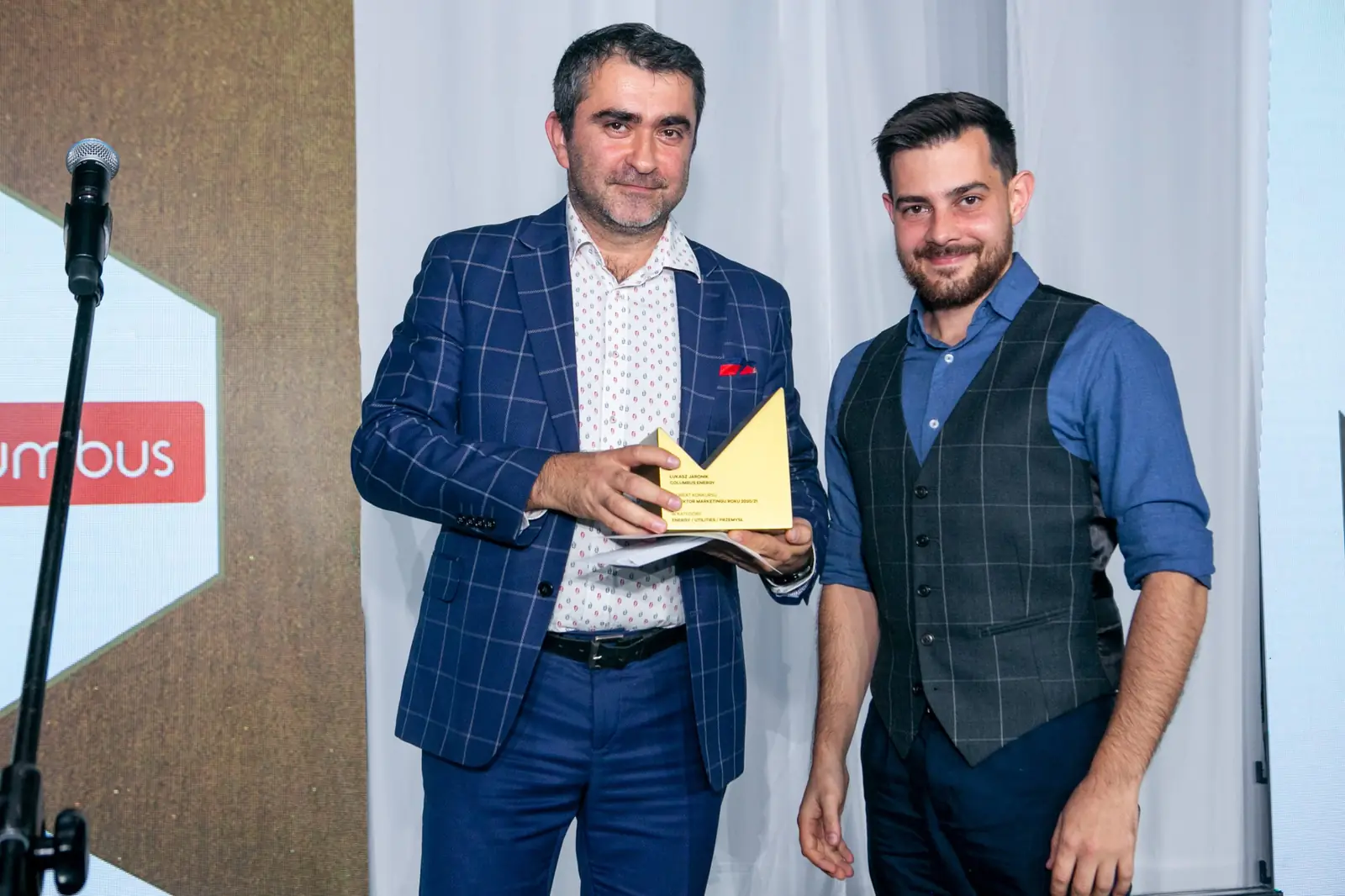 Winner in a waistcoat poses beside the presenter, who is still holding his statuette — DMR Gala X (2021)