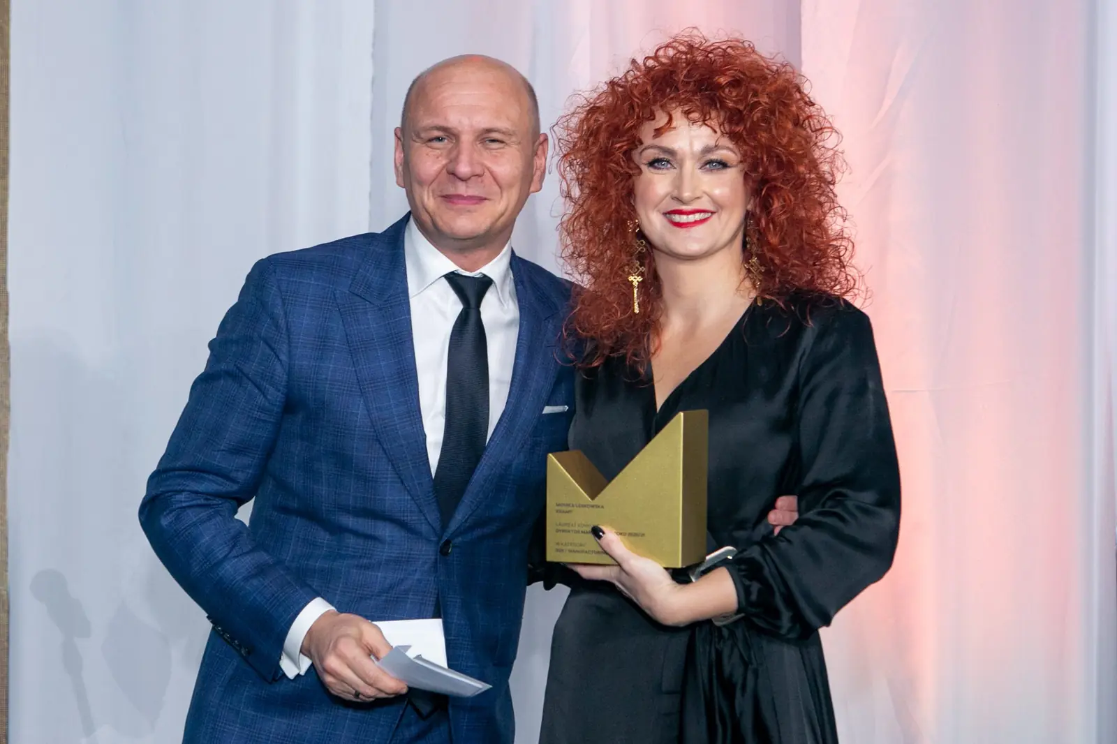 Laureatka z burzą rudych loków pozuje ze statuetką obok wręczającego w granatowym garniturze — Gala DMR X (2021)