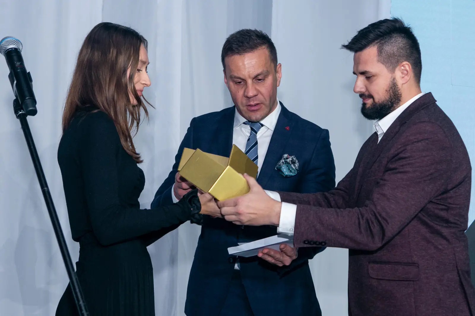 Asystentka i wręczający przekazują statuetkę brodatemu laureatowi w bordowej marynarce — Gala DMR X (2021)