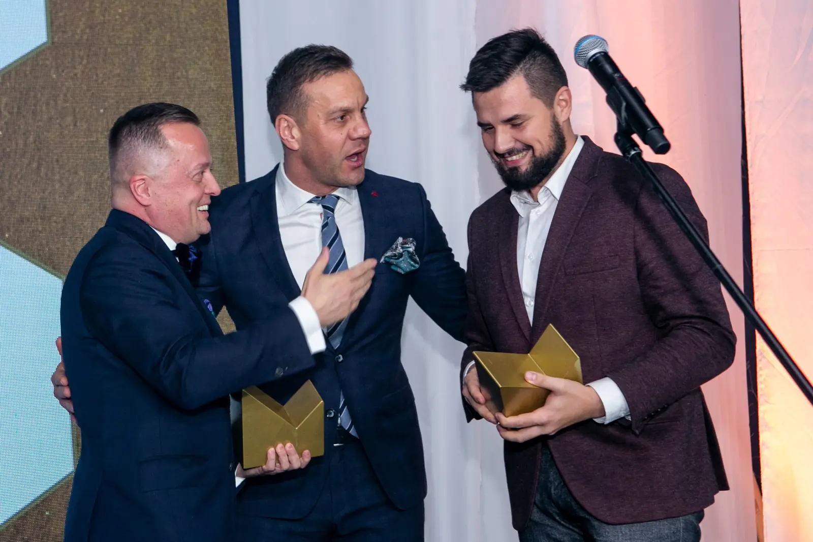 Trzej roześmiani mężczyźni ze statuetkami żartują razem na scenie — Gala DMR X (2021)