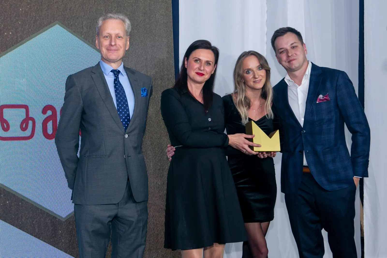 Three-person winning team with a statuette poses with the grey-haired presenter — DMR Gala X (2021)