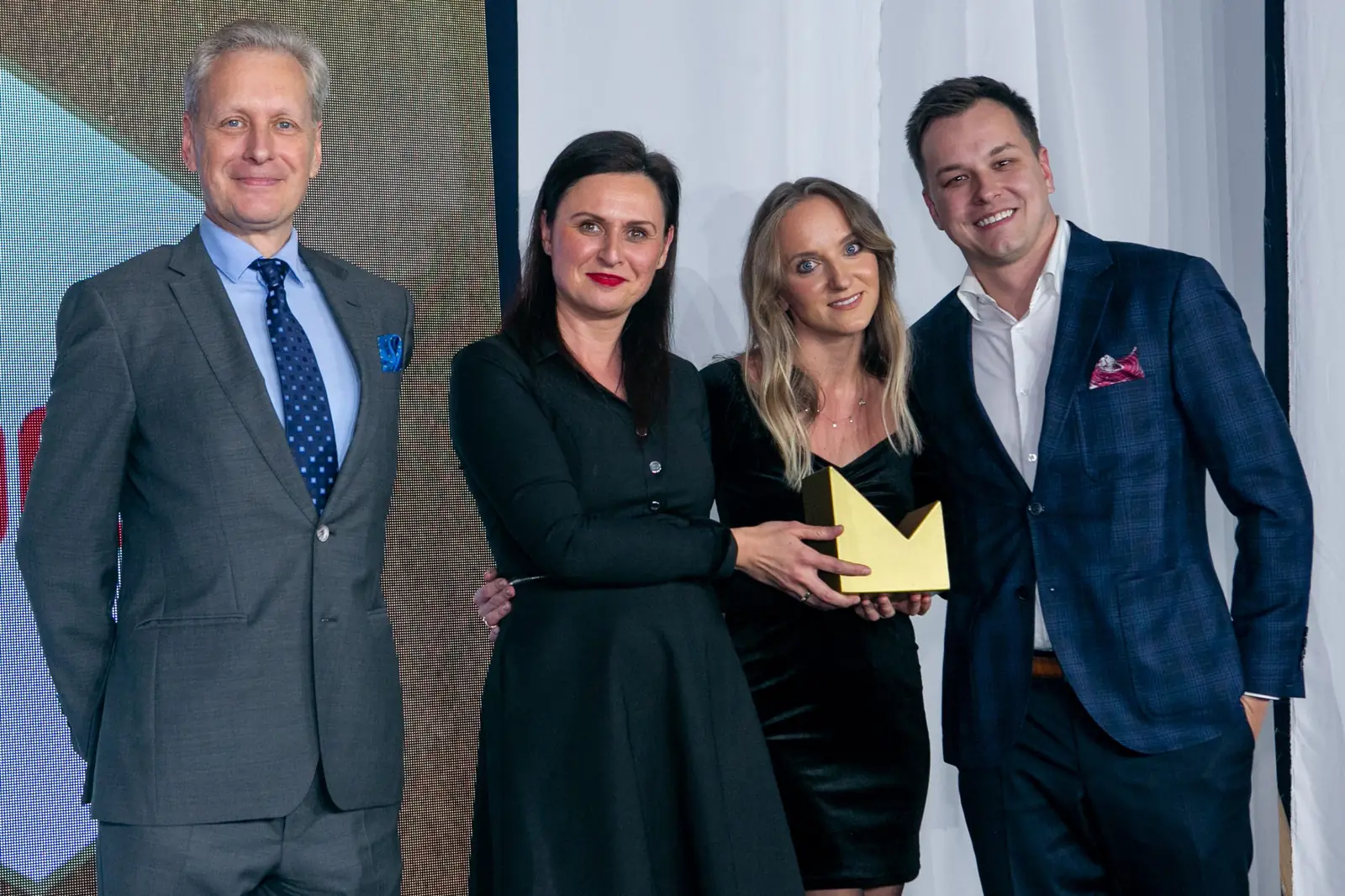 Dwie kobiety w czerni i mężczyzna w granatowej marynarce pozują ze statuetką obok wręczającego — Gala DMR X (2021)