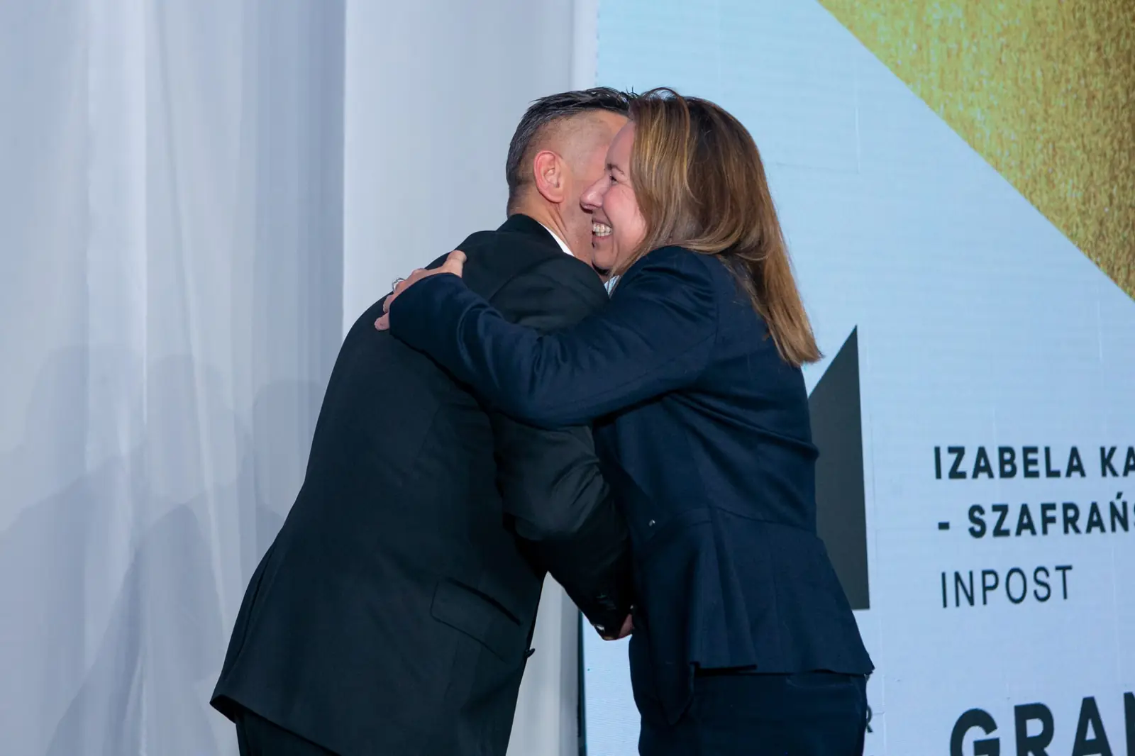 Prowadzący serdecznie ściska laureatkę Grand Prix w granatowej marynarce — Gala DMR X (2021)