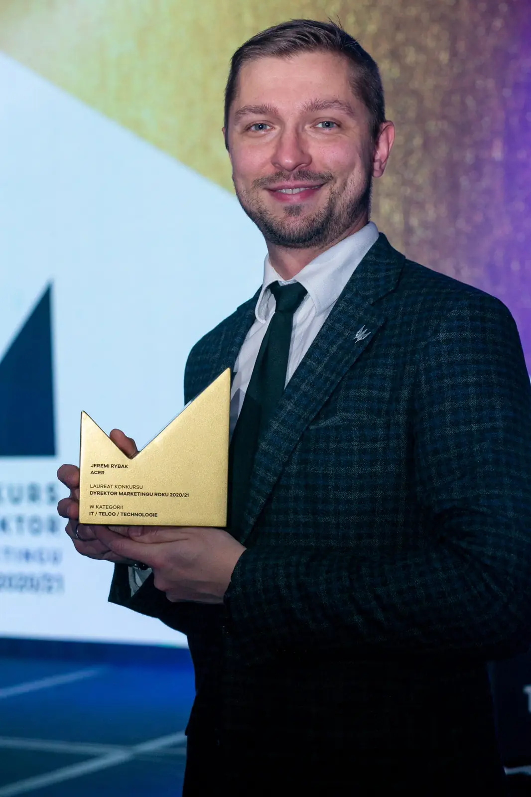 Smiling bearded winner in a dark checked jacket poses with a golden statuette — DMR Gala X (2021)