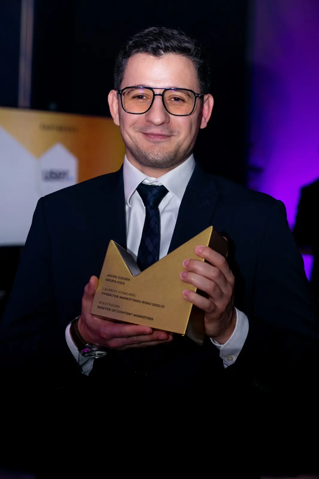 Young winner in glasses and a dark suit poses with his statuette against a dark background — DMR Gala X (2021)