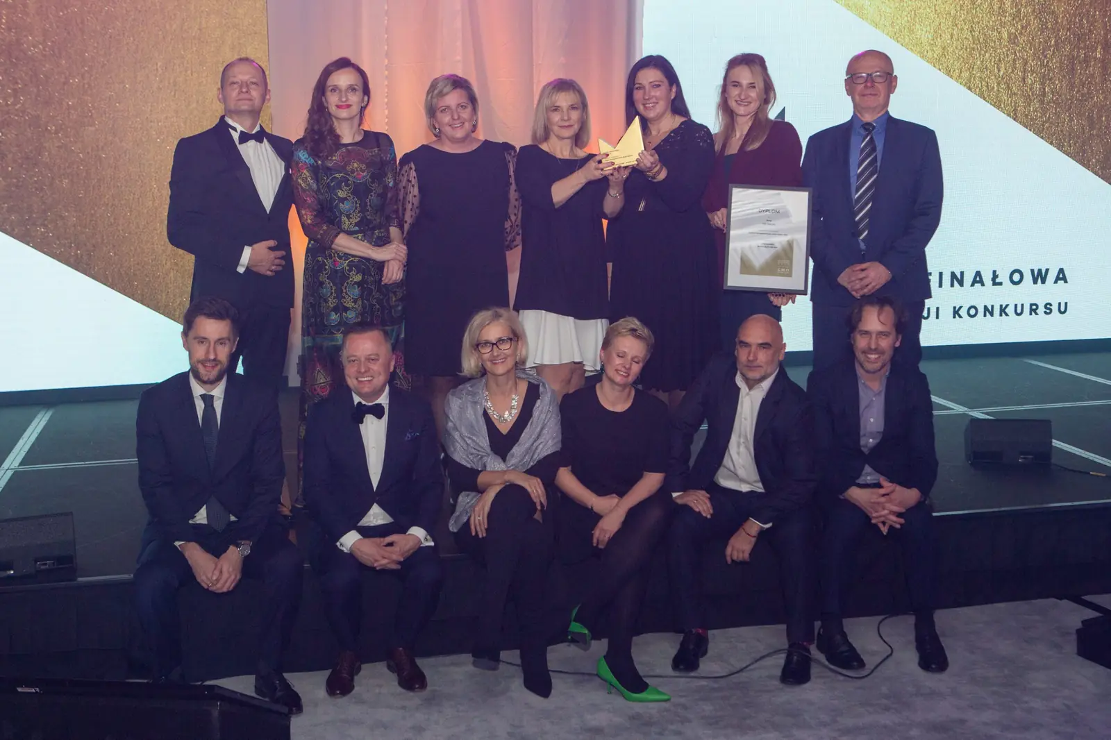 Group of twelve in two rows poses with a diploma and statuette in front of the gala screen — DMR Gala X (2021)