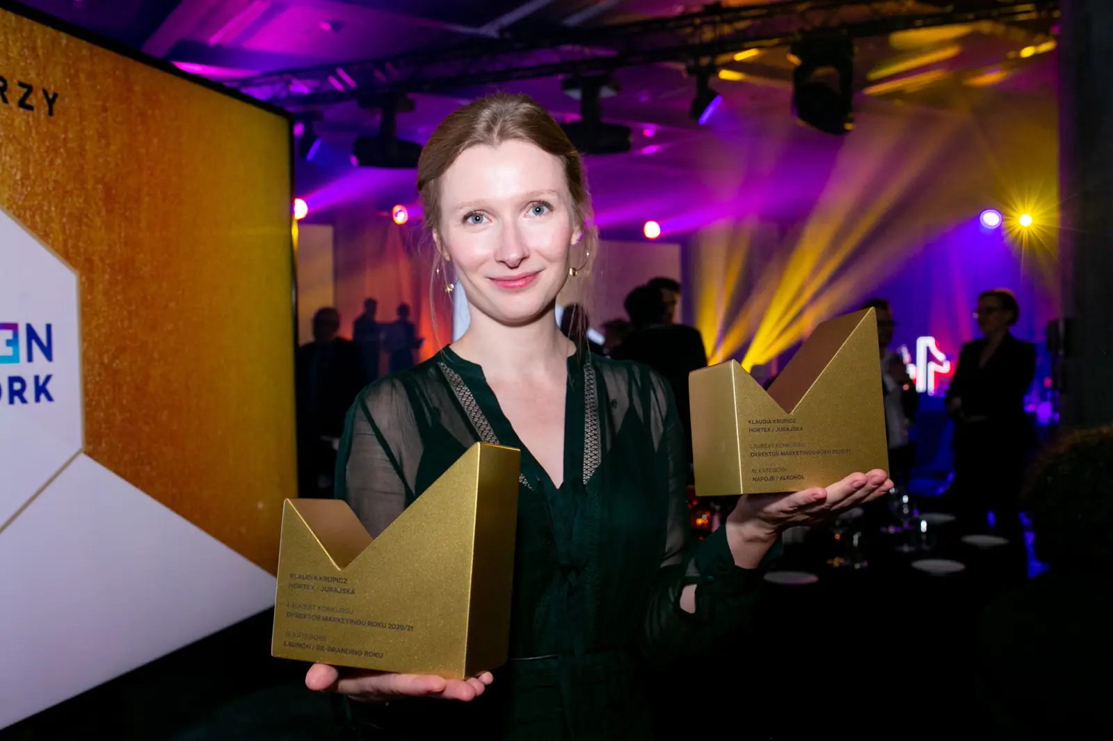 Winner in a dark green dress shows off two golden statuettes in the spotlight — DMR Gala X (2021)