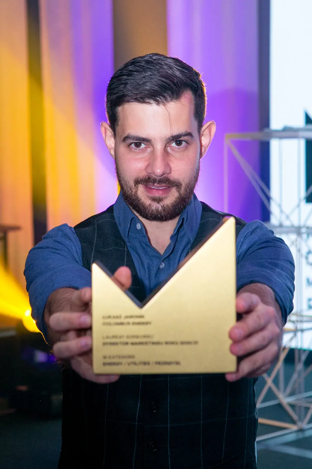 Winner in a waistcoat holds his golden statuette out towards the camera — DMR Gala X (2021)