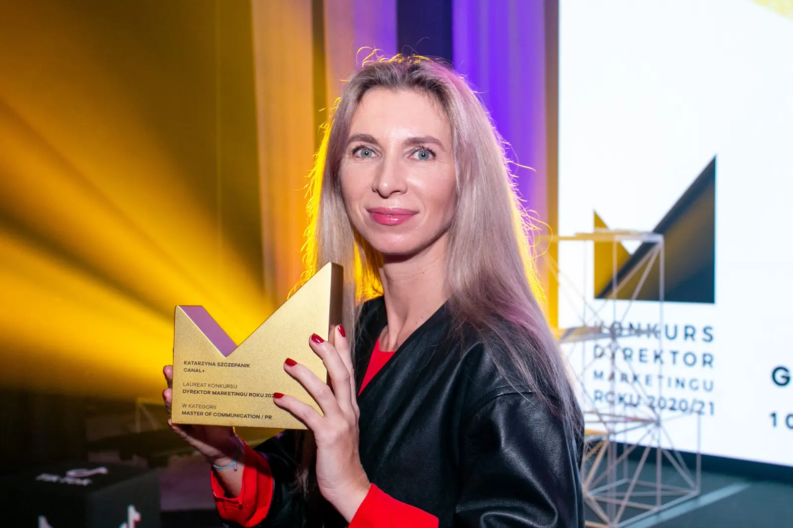 Laureatka o długich jasnych włosach pozuje ze statuetką na tle żółtych reflektorów — Gala DMR X (2021)