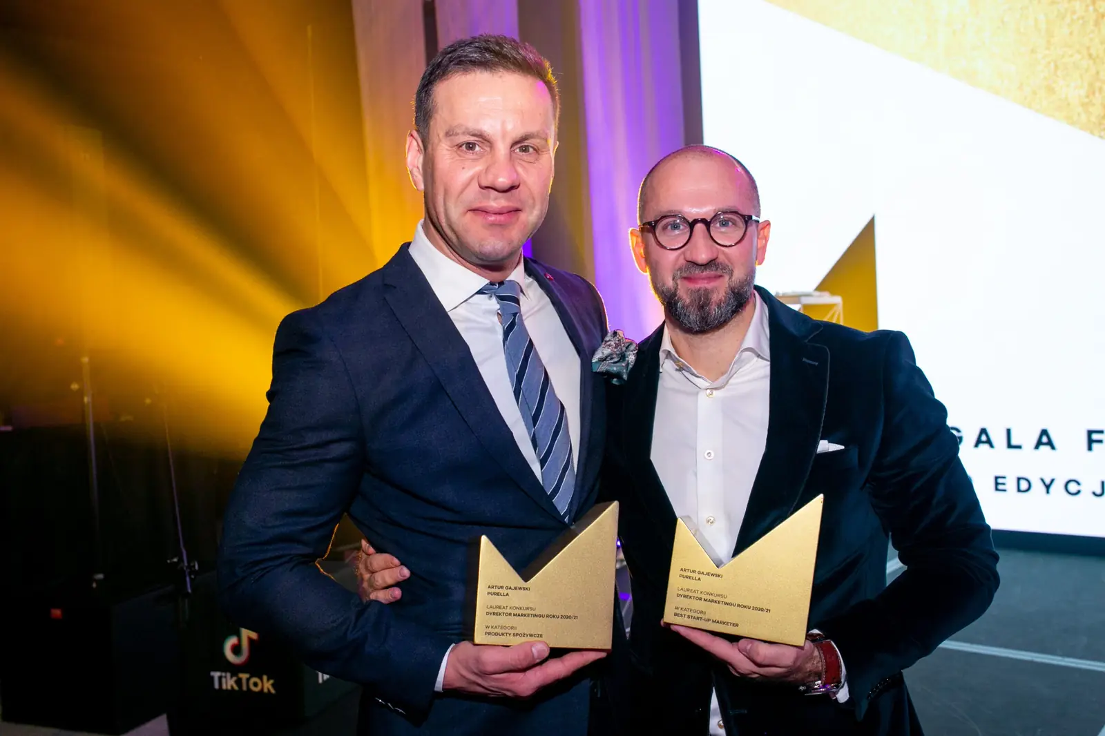 Two smiling winners in suits pose shoulder to shoulder with their statuettes — DMR Gala X (2021)