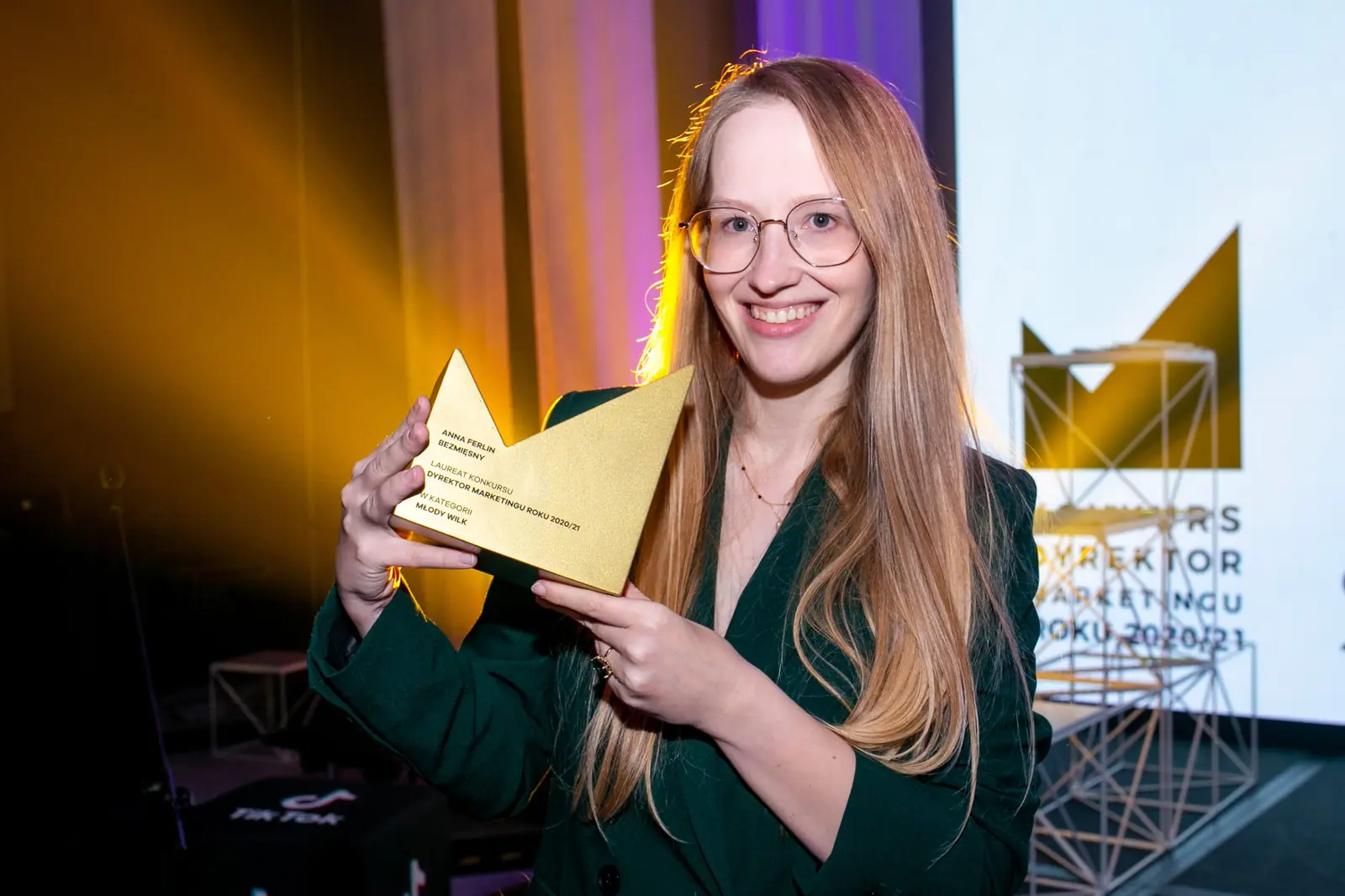 Młoda laureatka w okularach i zielonej marynarce z uśmiechem trzyma statuetkę — Gala DMR X (2021)
