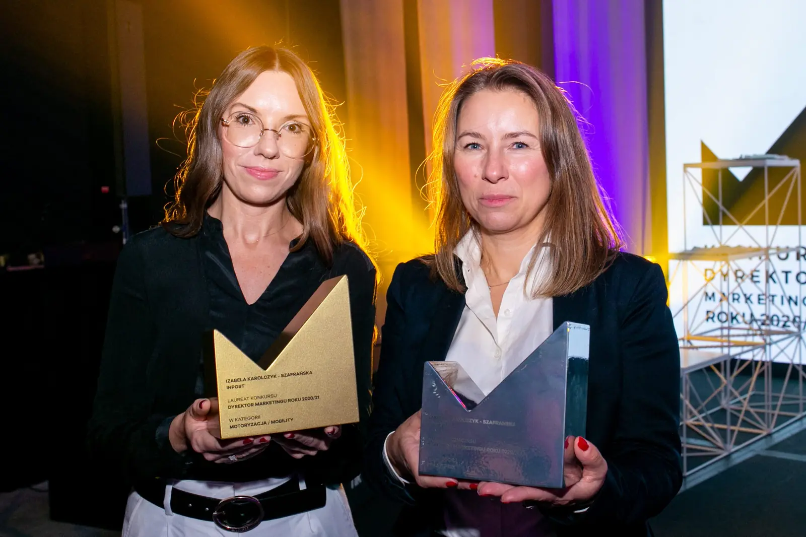 Two winners pose with a golden and a glass statuette against the stage structure — DMR Gala X (2021)
