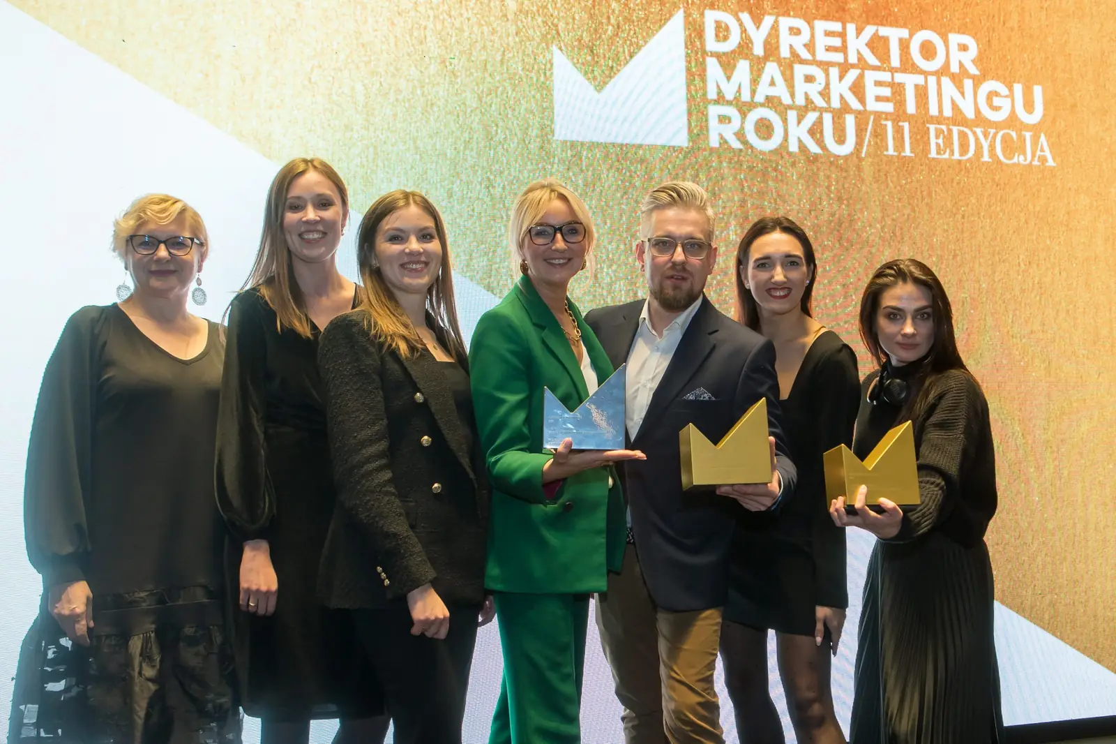 Siedmioosobowy zespół ze statuetkami pozuje przed złoto-białą ścianką konkursu — Gala DMR XI (2022)