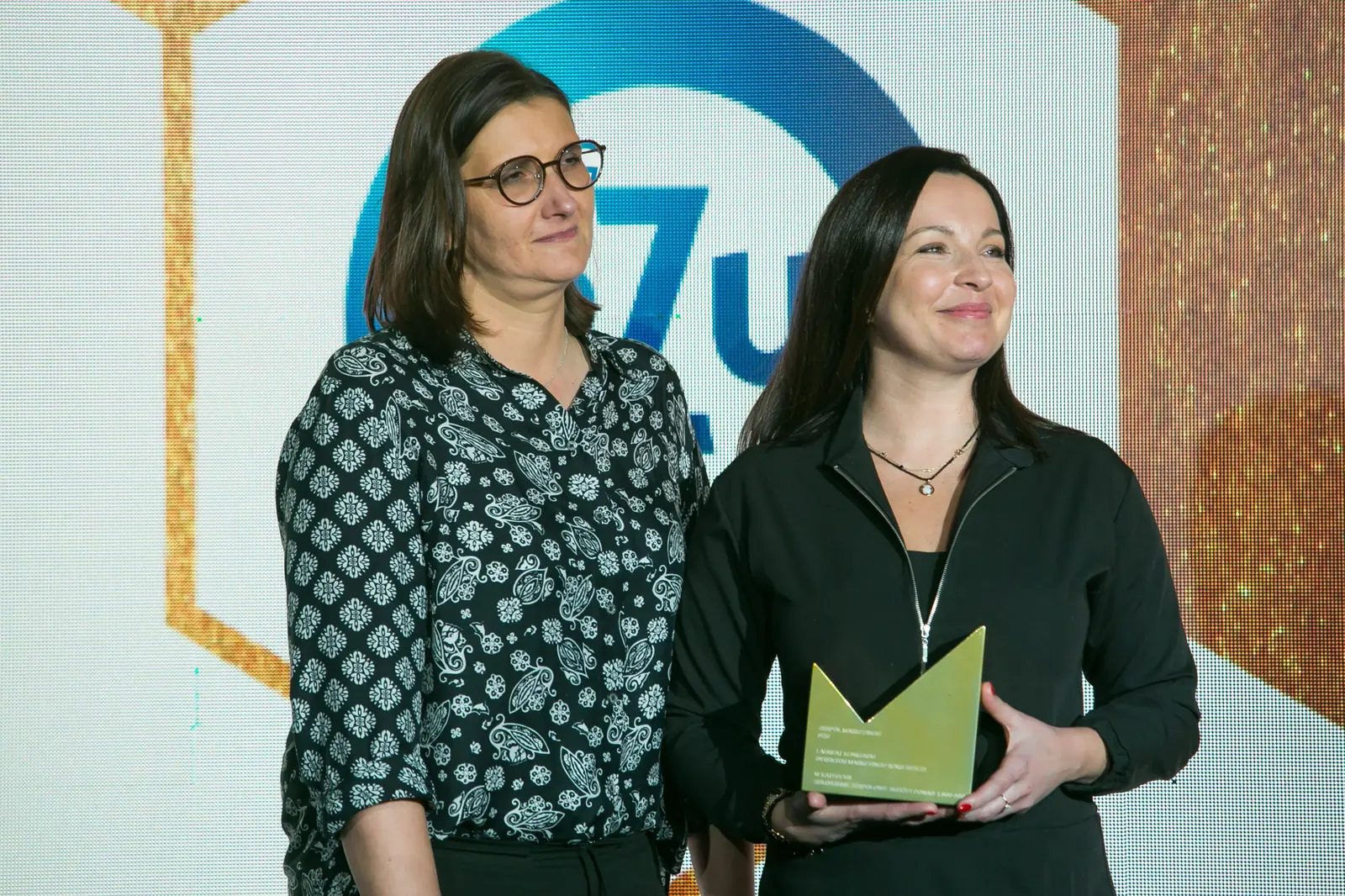 Dwie laureatki pozują ze złotą statuetką przed niebieskim logo firmy na scenie — Gala DMR XI (2022)