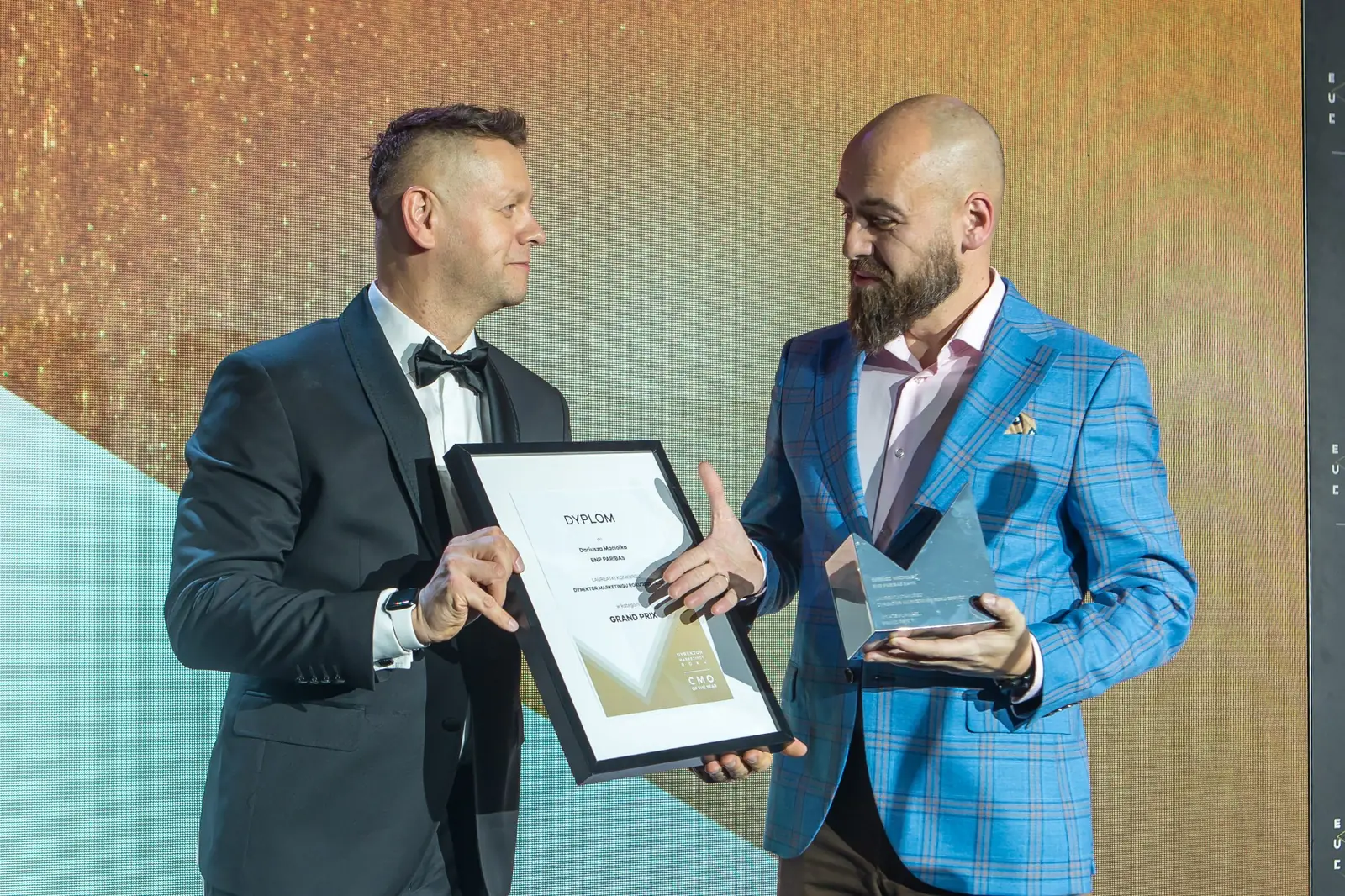 Laureat w niebieskiej marynarce odbiera dyplom od prowadzącego, trzymając już statuetkę — Gala DMR XI (2022)