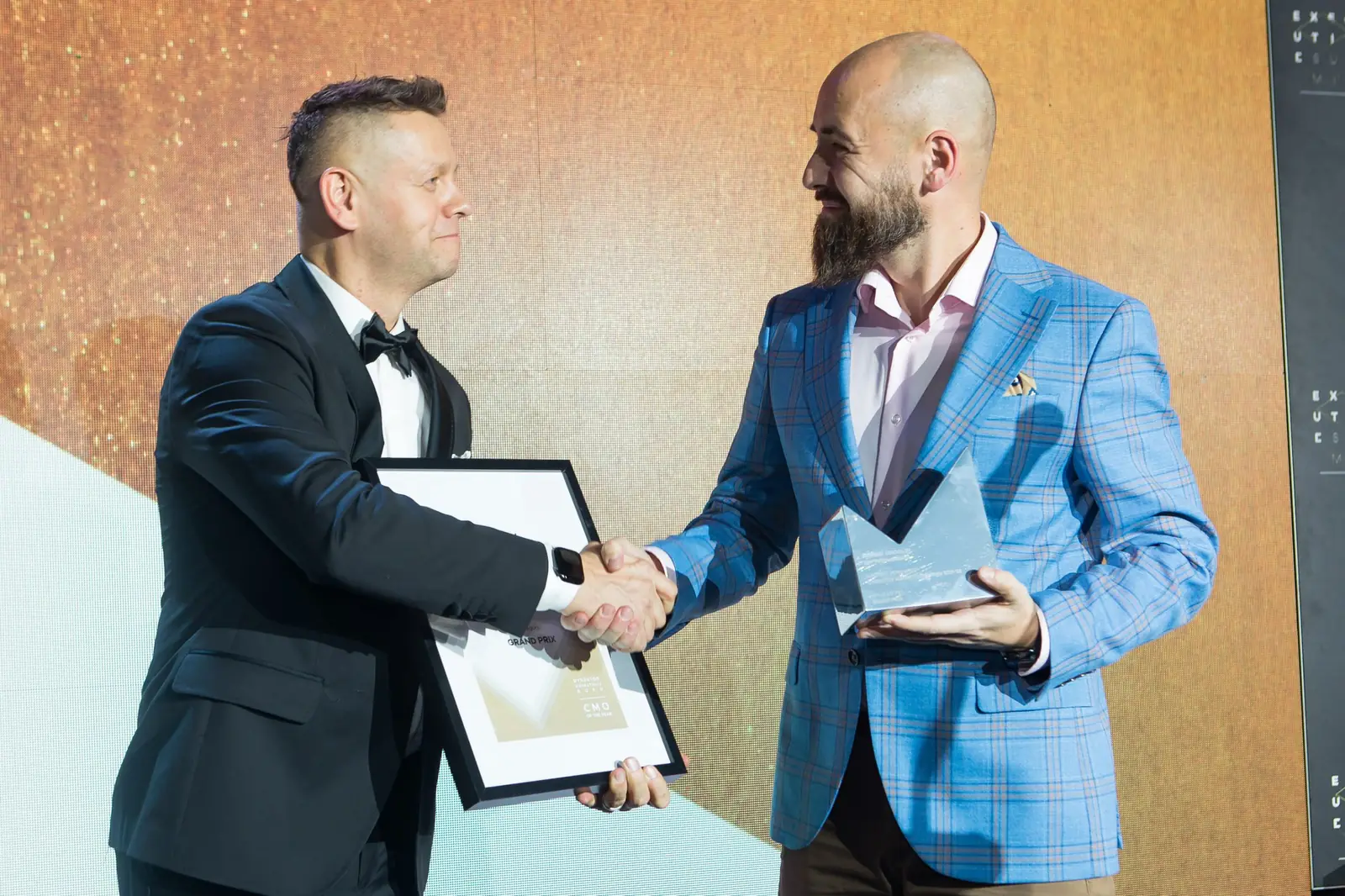 Prowadzący i laureat w niebieskiej marynarce ściskają sobie dłonie nad dyplomem — Gala DMR XI (2022)