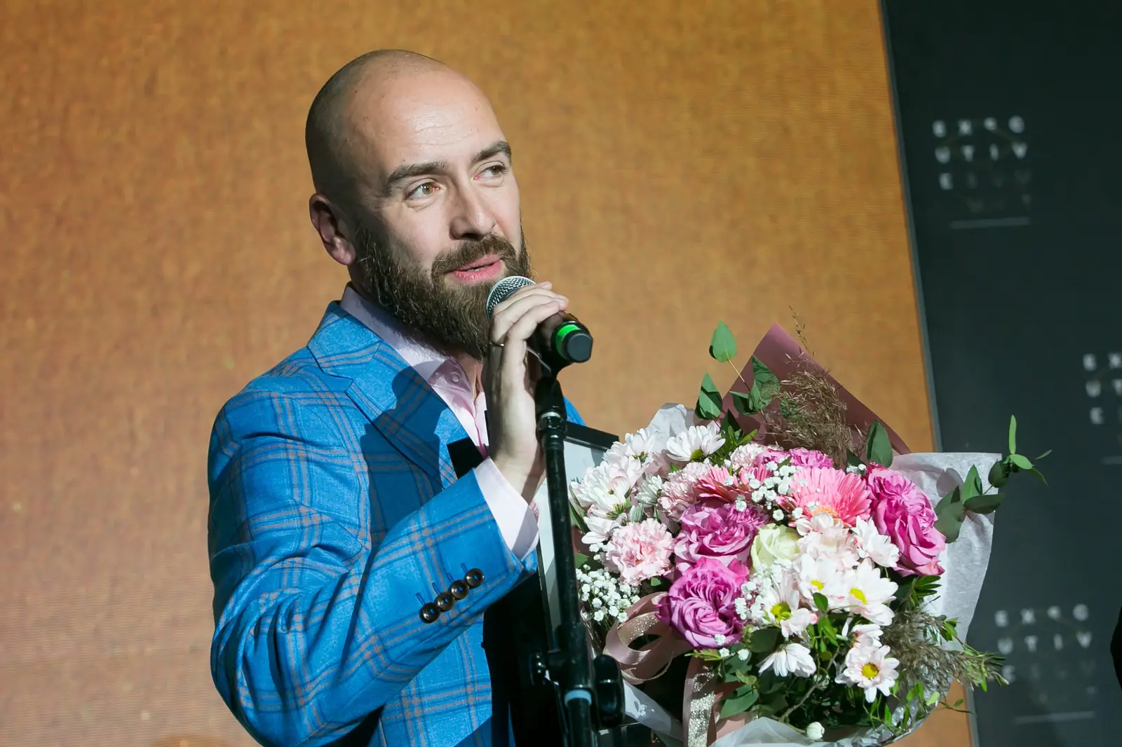 Laureat Grand Prix z brodą przemawia do mikrofonu, trzymając duży bukiet różowych kwiatów — Gala DMR XI (2022)