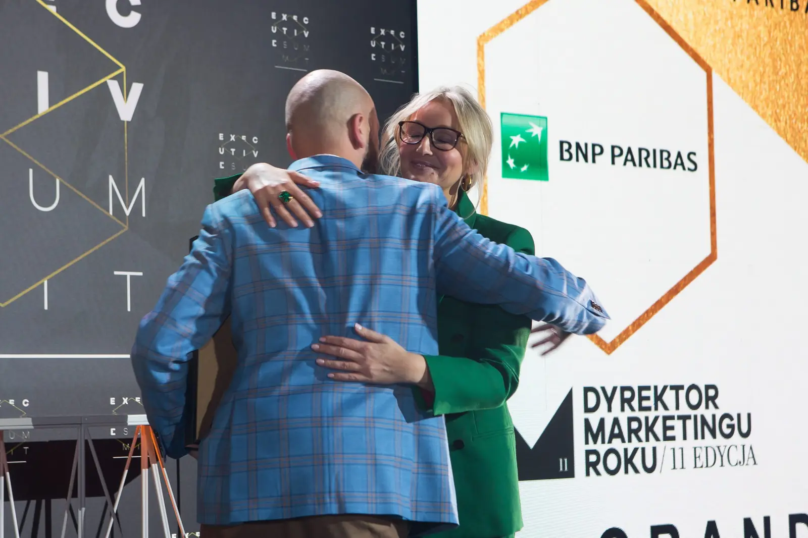 Laureaci Grand Prix serdecznie się obejmują: mężczyzna w niebieskiej marynarce i kobieta w zieleni — Gala DMR XI (2022)