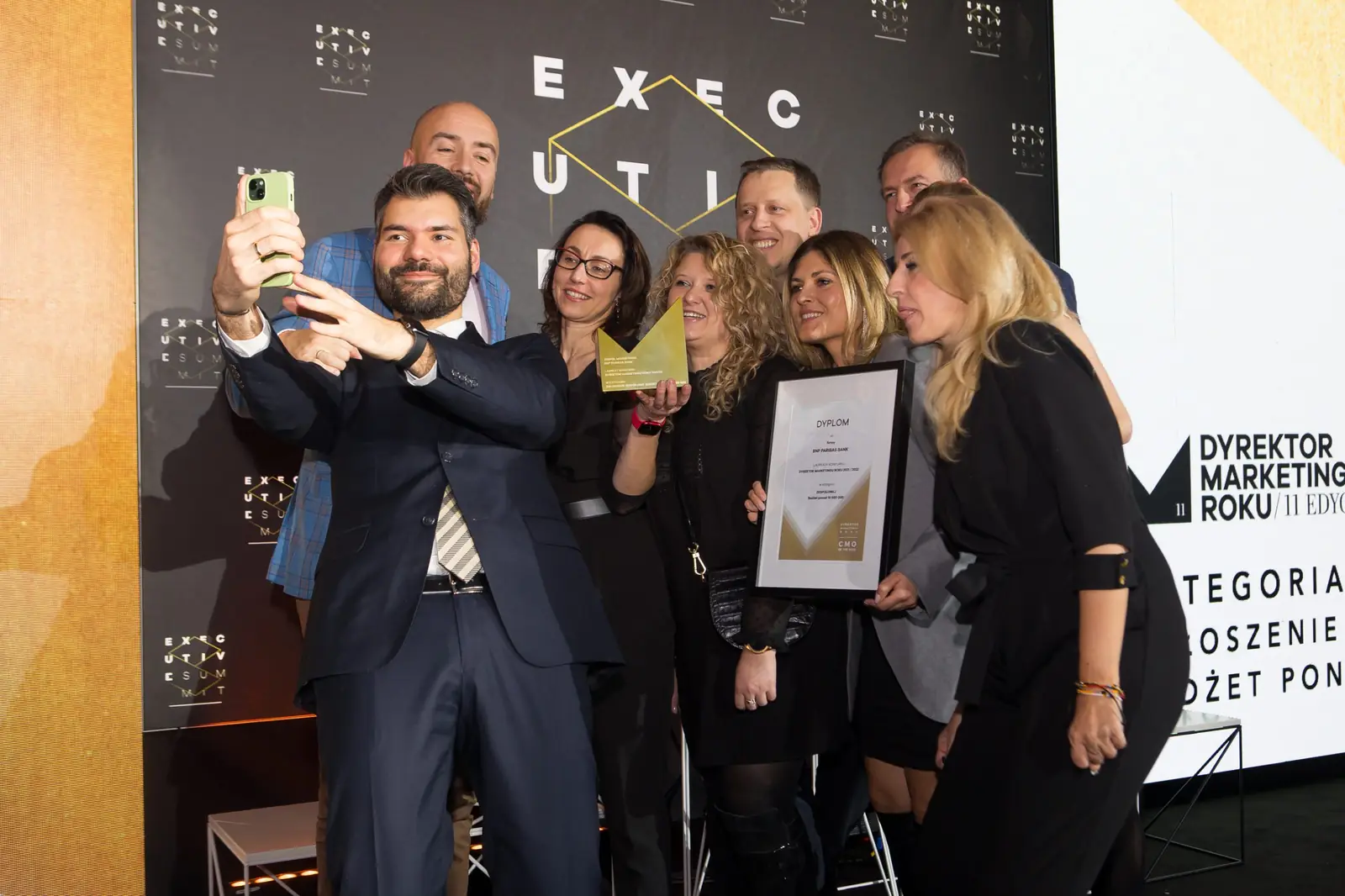 Laureat robi selfie z liczną grupą współpracowników przed ścianką wydarzenia — Gala DMR XI (2022)