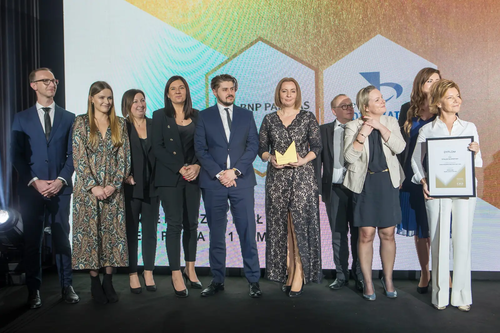 Jedenastoosobowa grupa laureatów ze statuetkami i dyplomami ustawiona w szeregu na scenie — Gala DMR XI (2022)