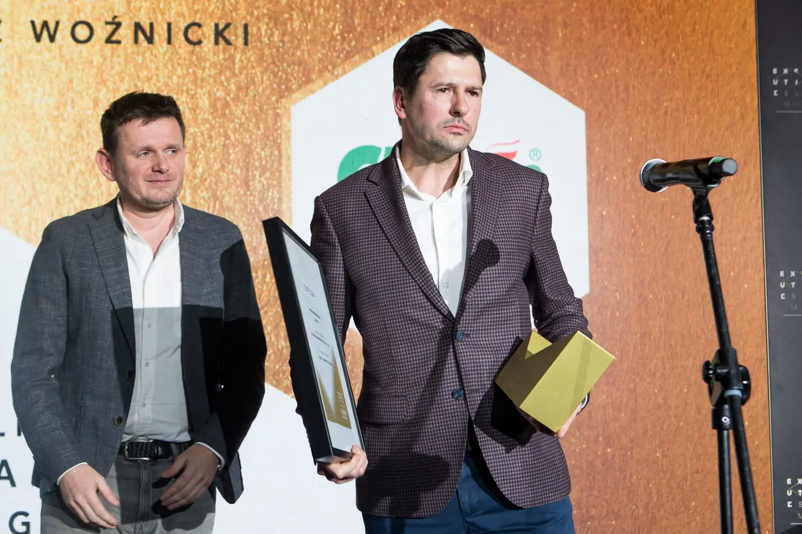 Laureat w brązowej marynarce z dyplomem i statuetką pozuje obok mężczyzny w szarej marynarce — Gala DMR XI (2022)