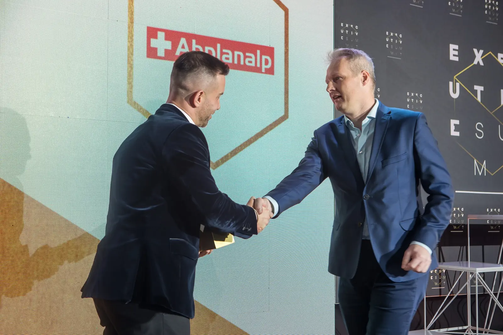 Mężczyzna w ciemnej marynarce ściska dłoń laureata w granatowym garniturze na scenie — Gala DMR XI (2022)