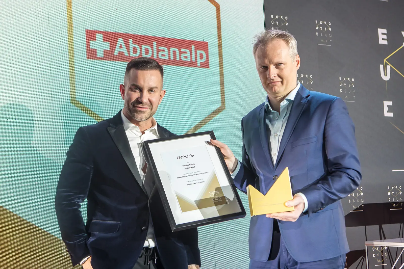 Laureat w granatowym garniturze pozuje ze złotą statuetką, a wręczający trzyma jego dyplom — Gala DMR XI (2022)